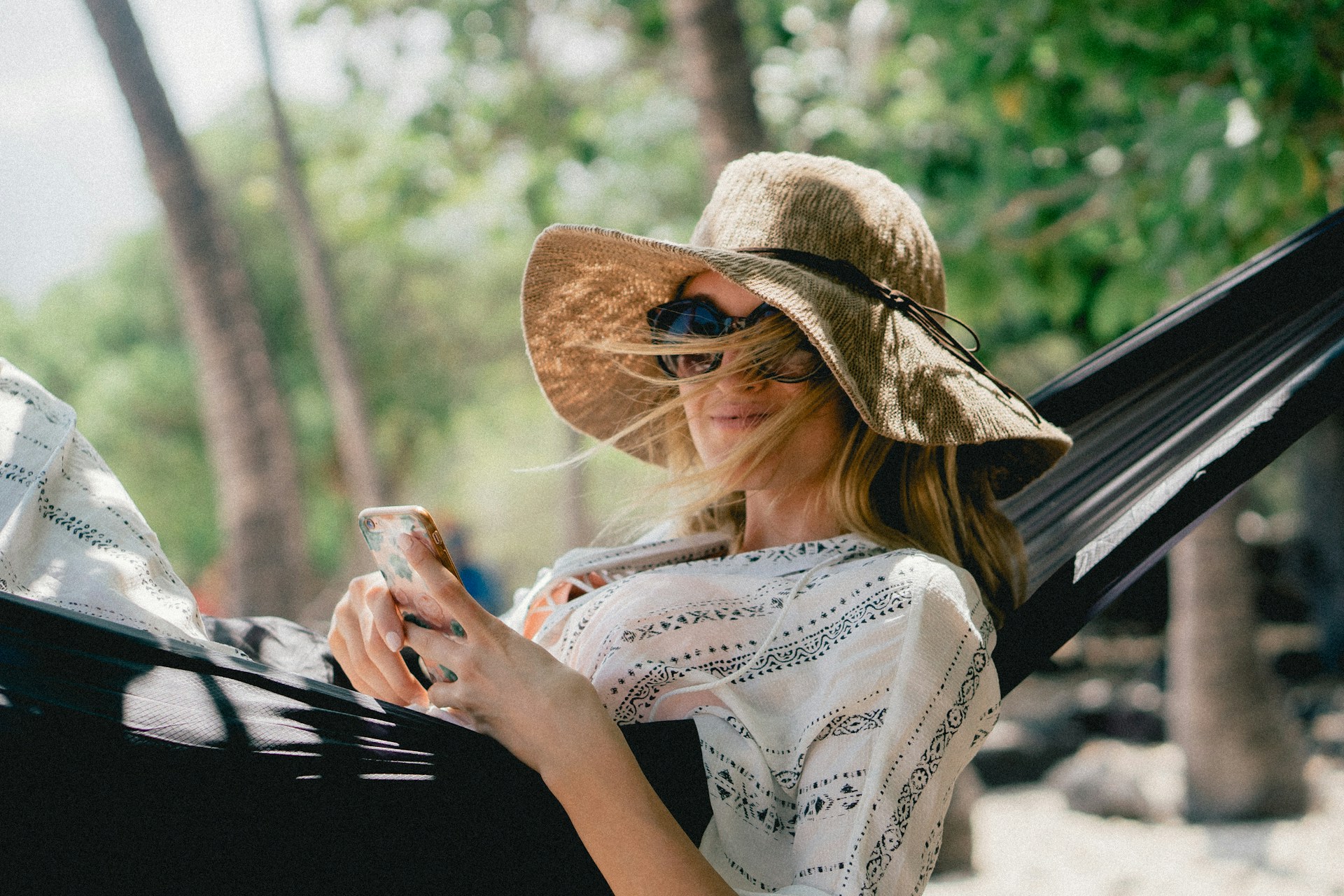 woman lying on black hammock while holding phone