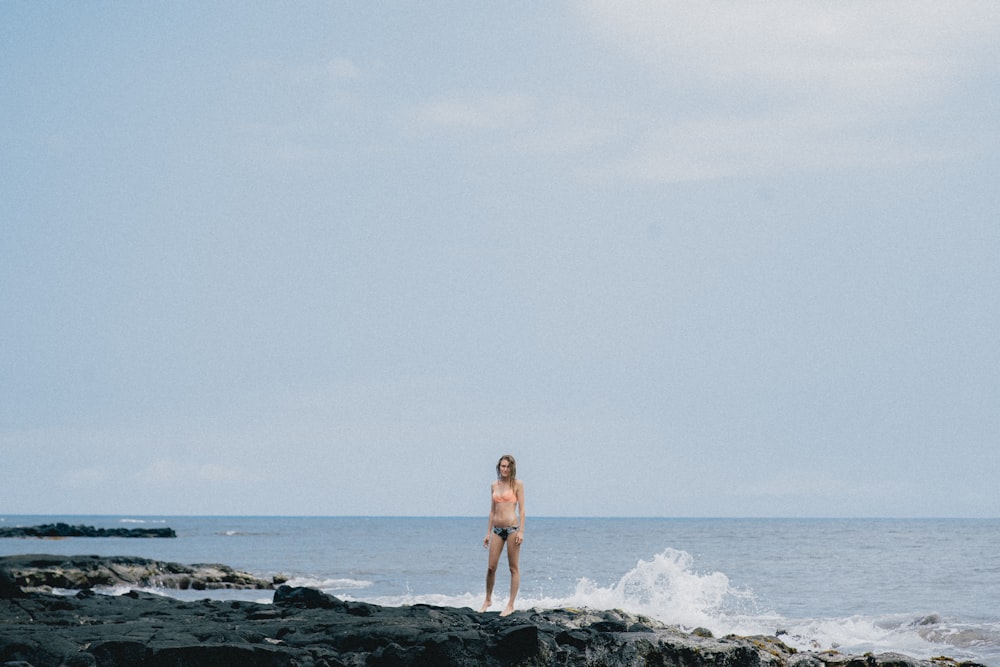Mujer de pie en una formación rocosa cerca del cuerpo de agua