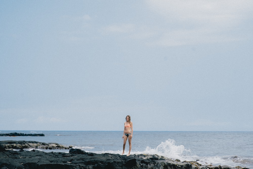 woman standing on rock formation near body of water