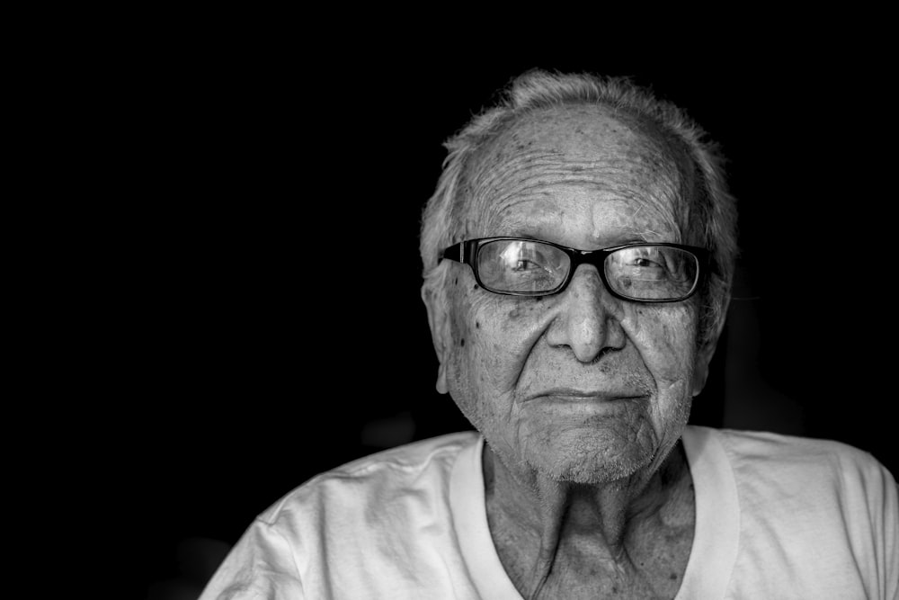 Photographie en niveaux de gris d’un homme portant une chemise et des lunettes