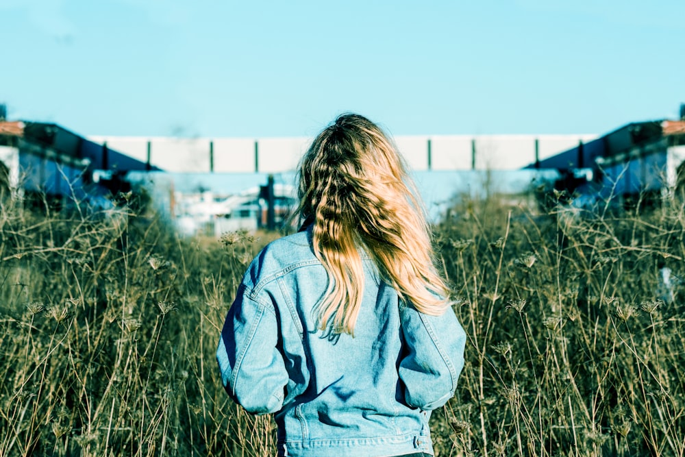 Frau in blauer Jeansjacke steht auf Rasenplatz