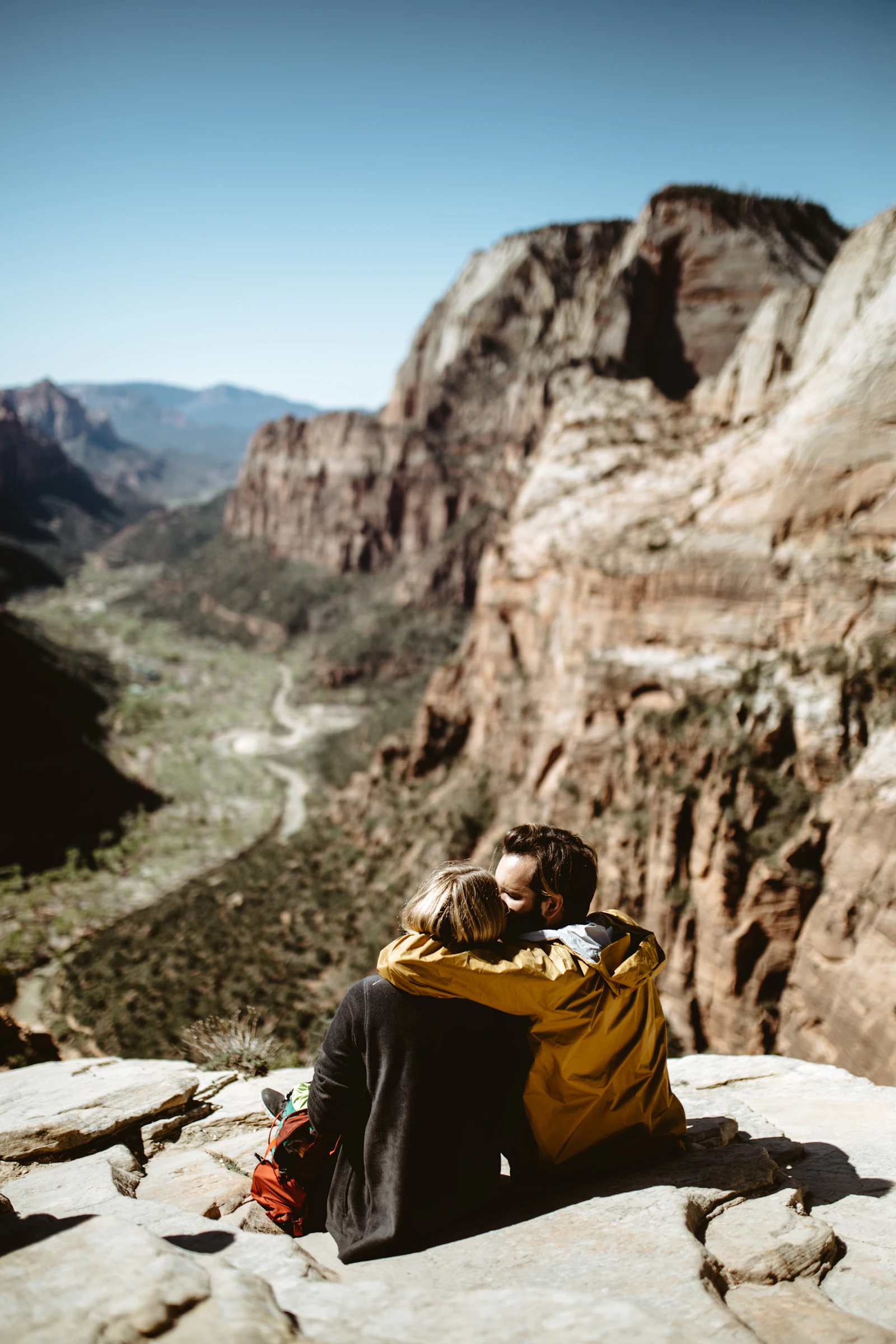 A couple sitting close together on a rock ledge above a canyon