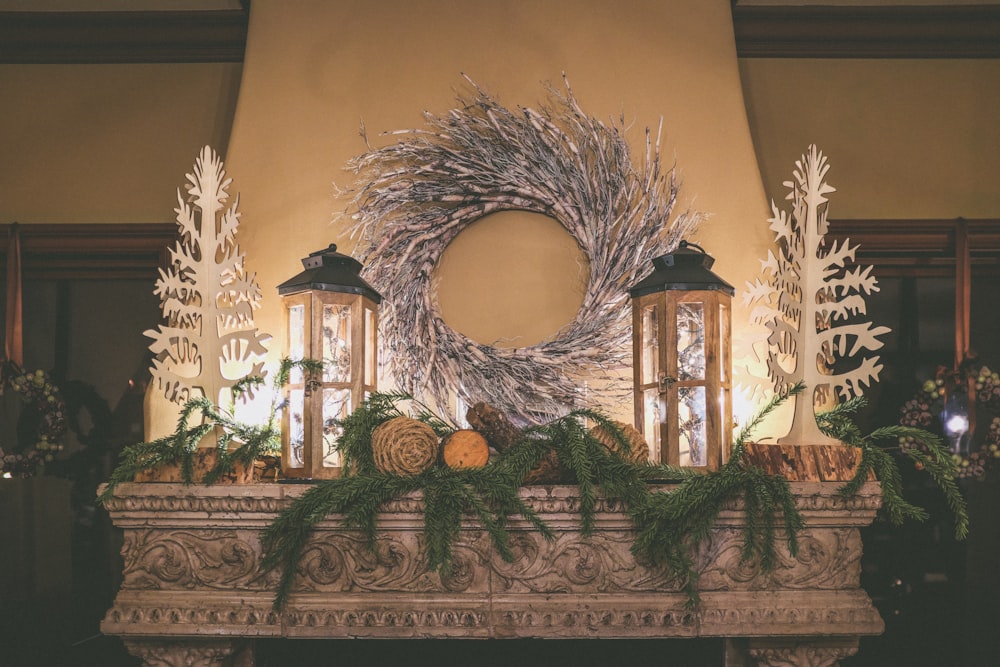 a mantle with a wreath and two lanterns on top of it