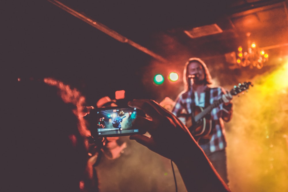 person taking photo of man playing guitar