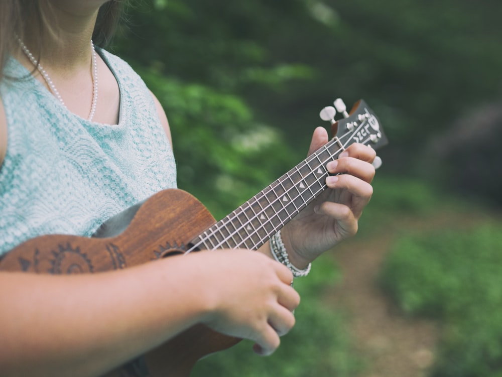 Frau trägt blaues ärmelloses Oberteil mit brauner Ukulele