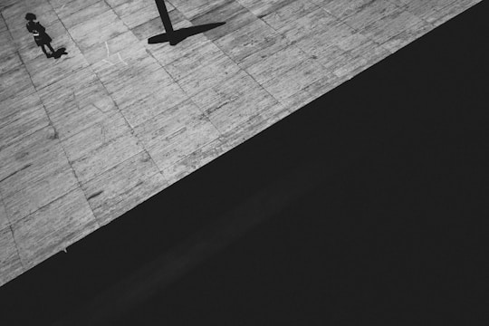 Black and white still of a lone figure framed by sharp geometric shadows.