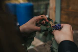 Hands gently arranging fresh herbs in a rustic ceramic vase on a wooden table.