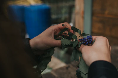 Hands gently arranging fresh herbs in a rustic ceramic vase on a wooden table.