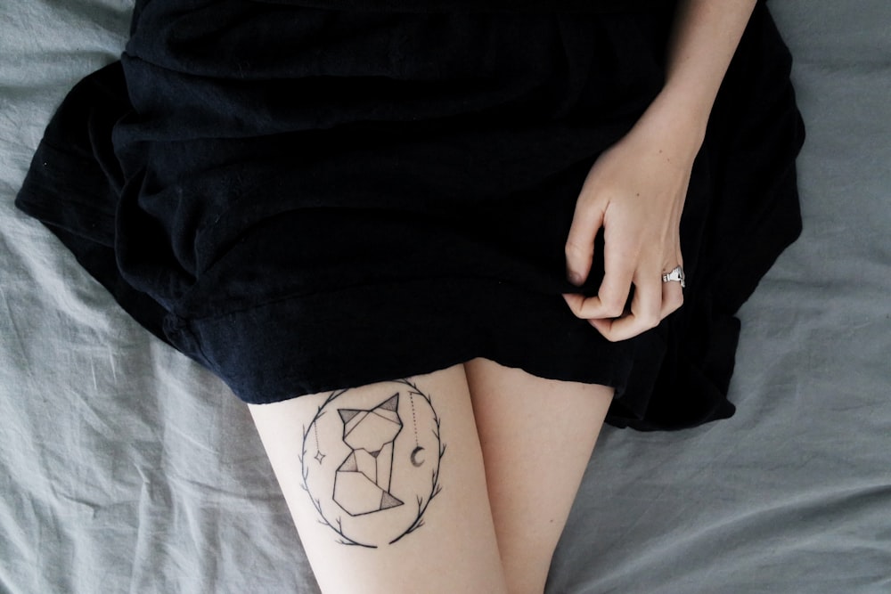 Frau, die tagsüber auf dem Bett liegt und Katze Dreamcatcher Tattoo auf dem rechten Bein sät