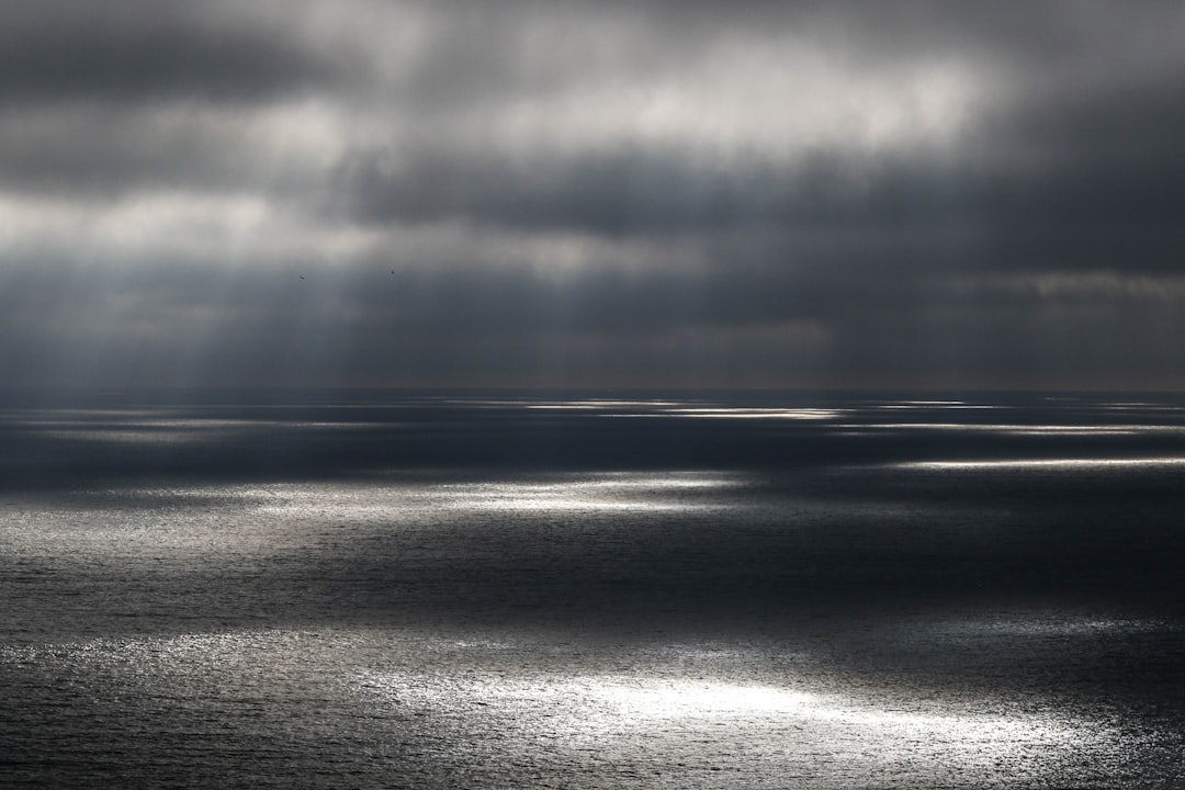 body of water under gray cloudy sky, I spotted these pockets of sunlight from the southern tip of San Diego and they wer