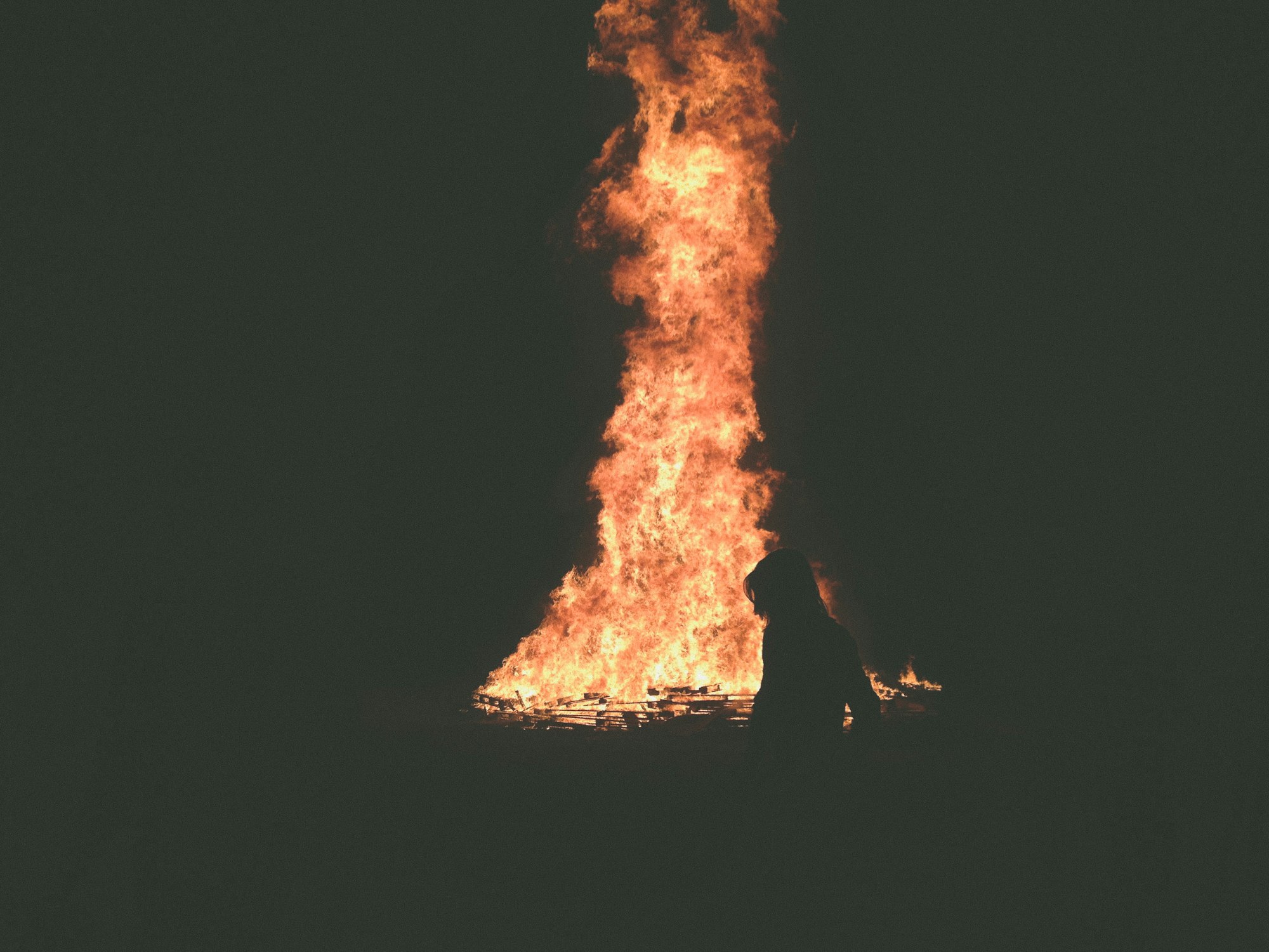 a woman's silhouette in front of a massive bonfire