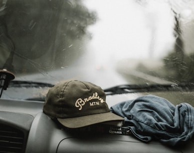 black and white baseball cap near grey shirt on top of glove compartment inside car