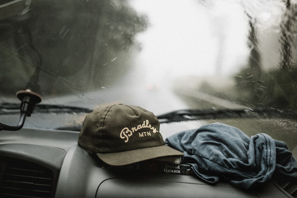 black and white baseball cap near grey shirt on top of glove compartment inside car