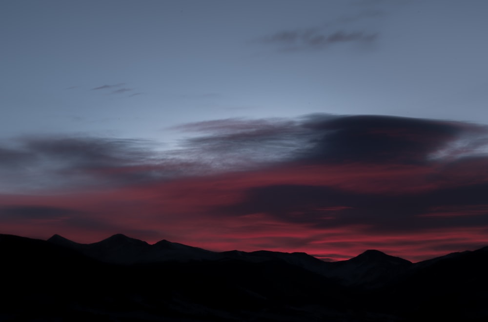 a red and blue sky with mountains in the background
