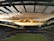 A large stadium filled with spectators watching a soccer match. The field is brightly lit, and the players are in action. Above the stadium, dramatic clouds in shades of orange and yellow stretch across the sky as the sun begins to set.
