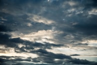 Dark, dense clouds fill the sky, with varying shades of gray and hints of light breaking through, suggesting an overcast or stormy weather condition. The atmosphere appears moody and dramatic as the clouds move across the horizon.