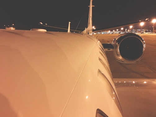 A jet engine close-up with reflections of the runway lights during dusk.