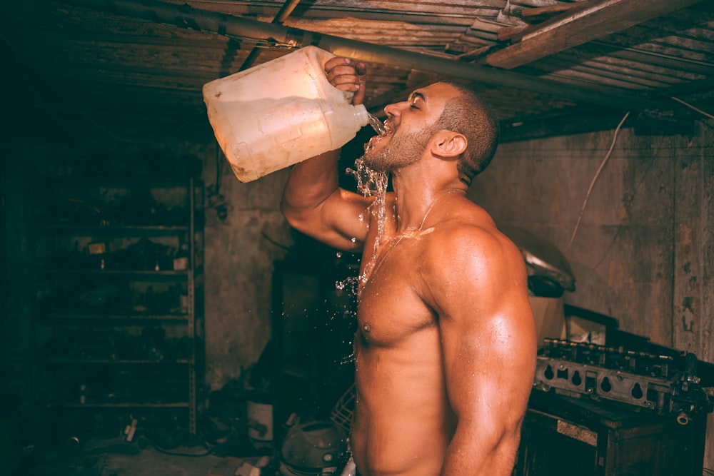 uomo in topless che beve acqua da un contenitore di plastica