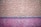 The image features a textured wall with abstract patterns. The upper portion of the wall is painted in a beige color, while the lower portion is pink, separated by a thin blue line. The surface has rough, uneven protrusions giving it a rustic, unfinished look.