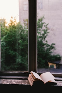 An open book resting on a windowsill overlooking a peaceful garden