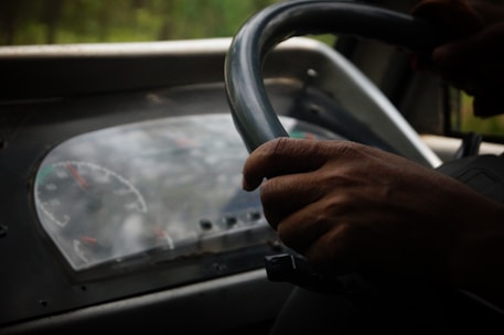 A close-up of hands on a steering wheel with a road ahead.