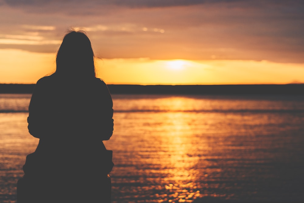 silhouette di donna seduta vicino alla baia