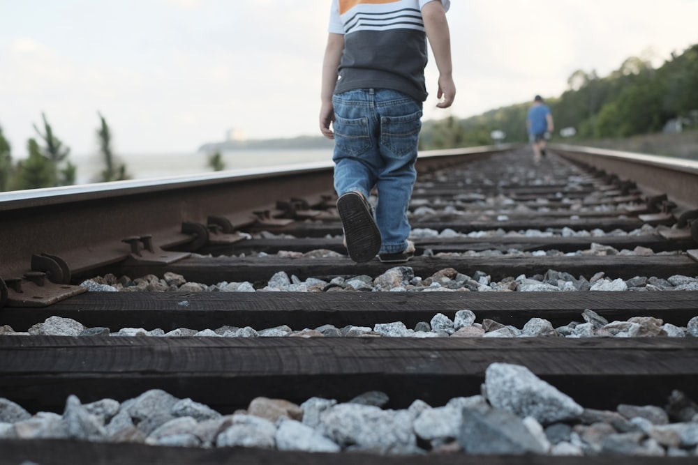 toddler walking on train rail during daytime
