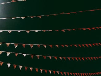 Several strings of triangular pennant flags, alternating in red and white, are hanging against a dark background. The flags are evenly spaced and appear to be part of a festive or celebratory setting.