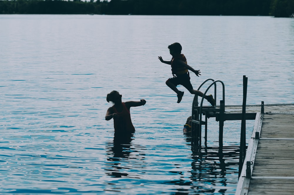 fotografia do menino saltando no corpo da água durante o dia
