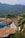 A picturesque view of a vibrant town nestled against a backdrop of lush green mountains. The foreground features a series of colorful colonial-style buildings with tiled roofs, set along a narrow, cobblestone street. Palm trees and greenery add to the tropical ambiance.