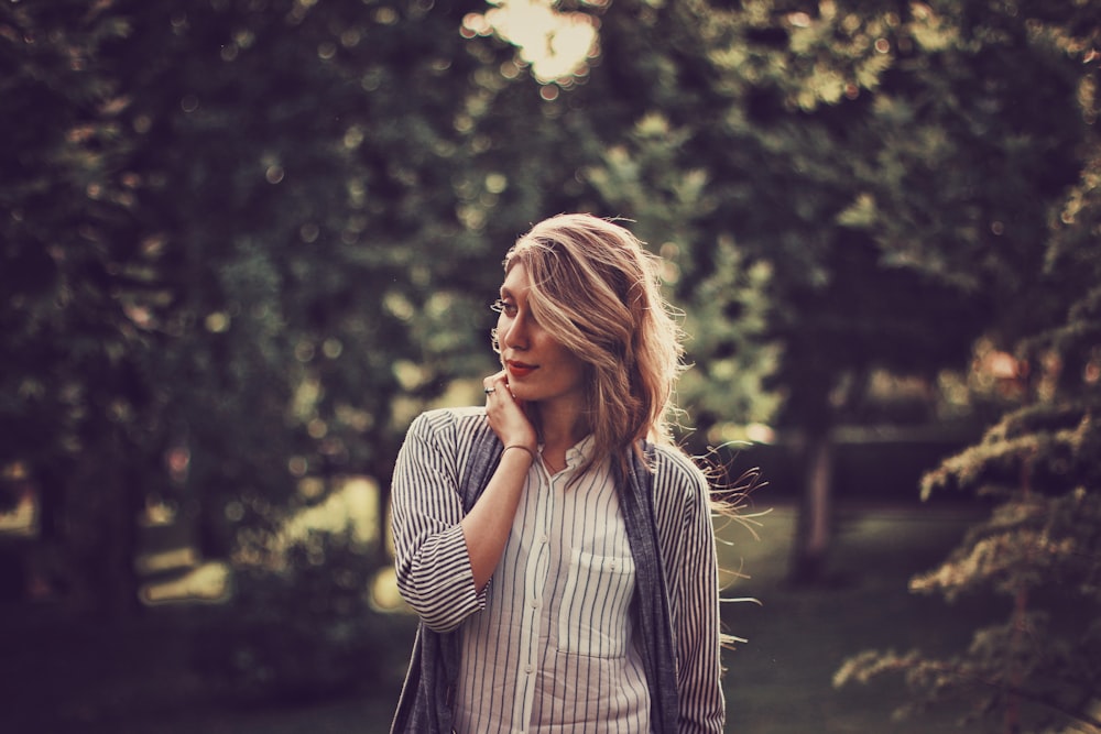 A woman wearing a striped shirt smiles to the side in front of trees