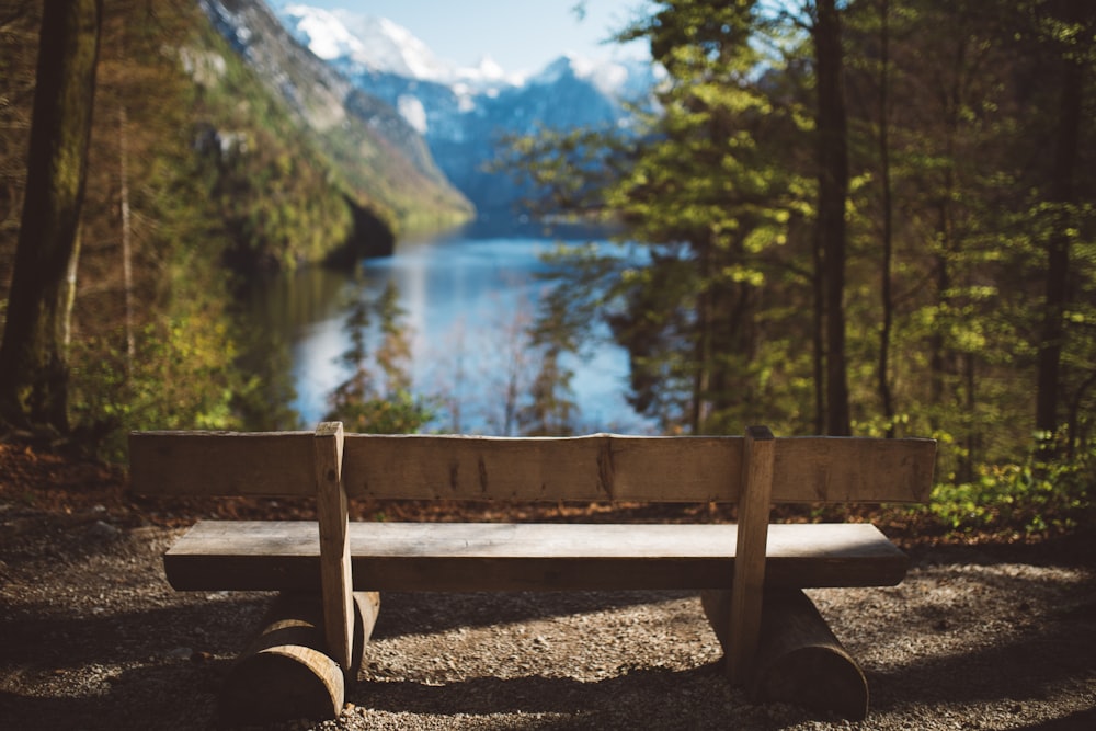 empty brown wooden bench facing body of water and mountain