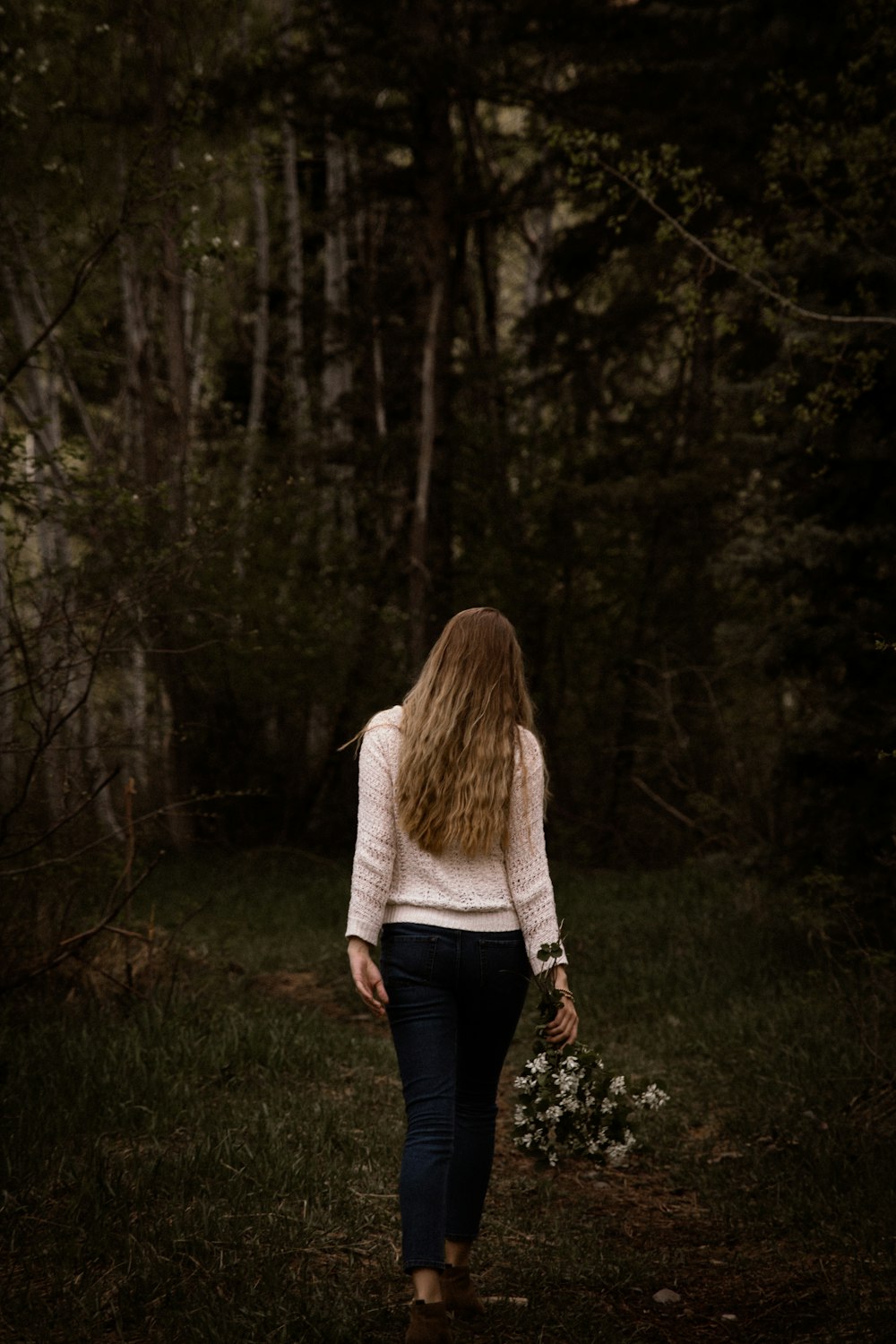 白いセーターと黒いズボンを着た女性が木の近くを歩く