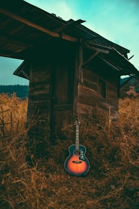A rustic guitar resting against a weathered wooden fence under a wide Texas sky at sunset.