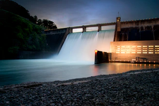 A large dam reservoir with water flowing over the spillway at sunset.
