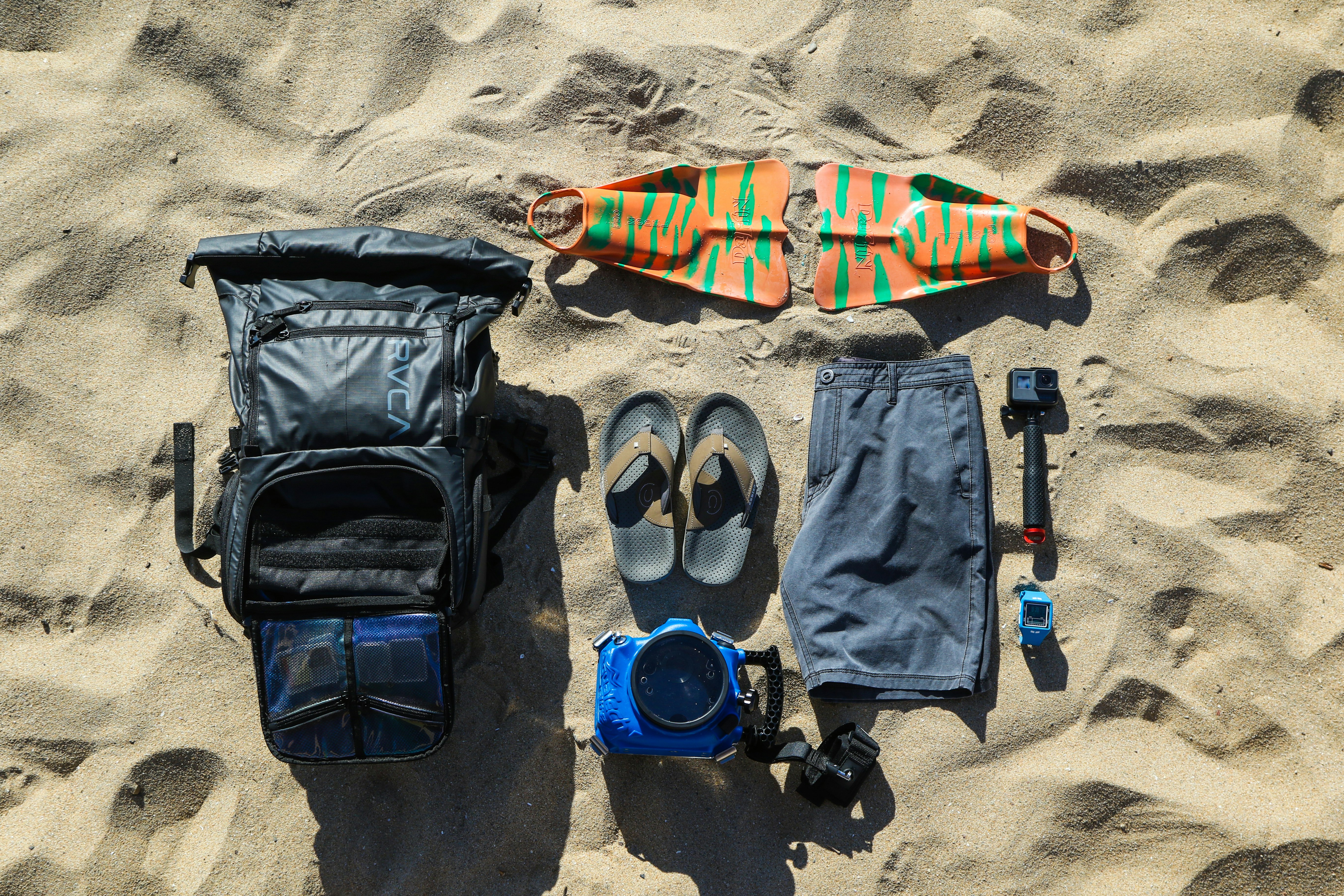 flat-lay photography of flip-flops, hiking backpack, board, shorts, and action camera