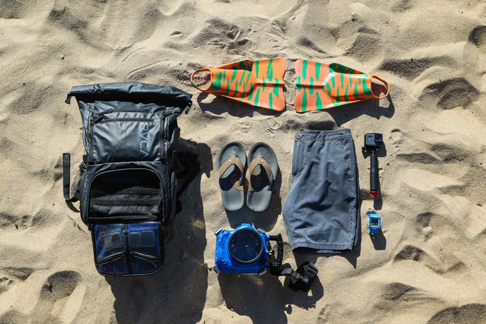 flat-lay photography of flip-flops, hiking backpack, board, shorts, and action camera