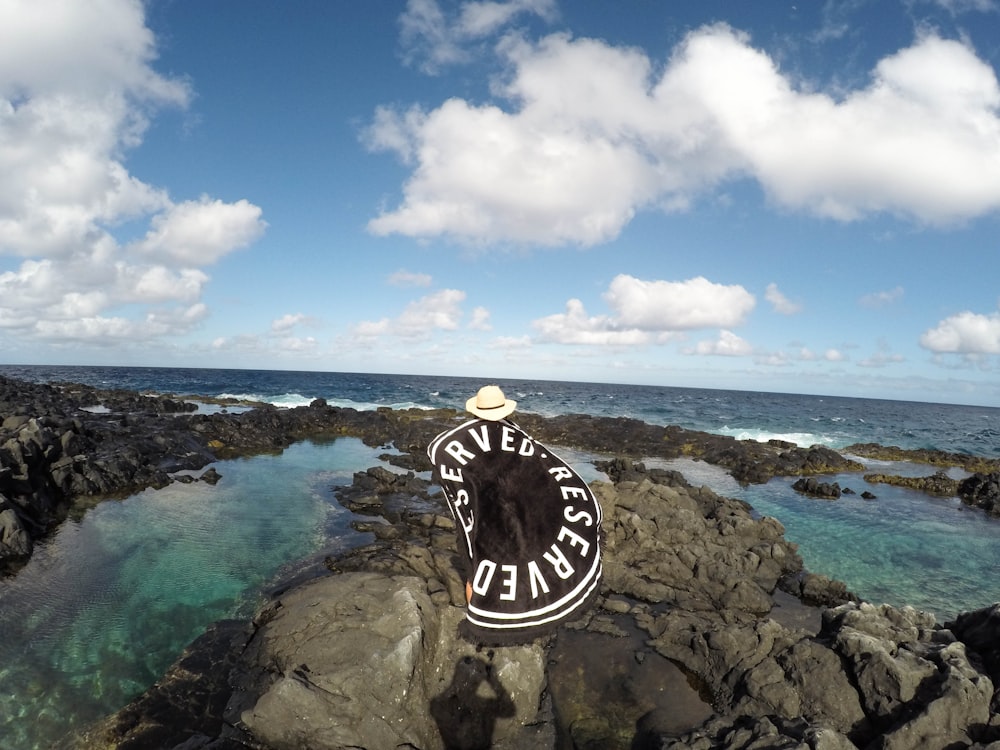 black and white cap on brown rock formation near sea under blue sky during daytime