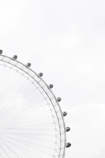 Part of a ferris wheel with enclosed cars for riding in and people in the cars against an overcast sky