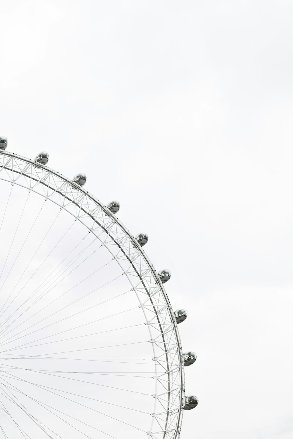 Part of a ferris wheel with enclosed cars for riding in and people in the cars against an overcast sky