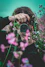 selective focus of woman behind pink flowers holding red Samsung bridge camera about to take photo of flower