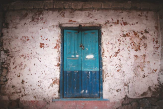 Close-up of a weathered wooden door with peeling paint and rusty hinges, evoking nostalgia.