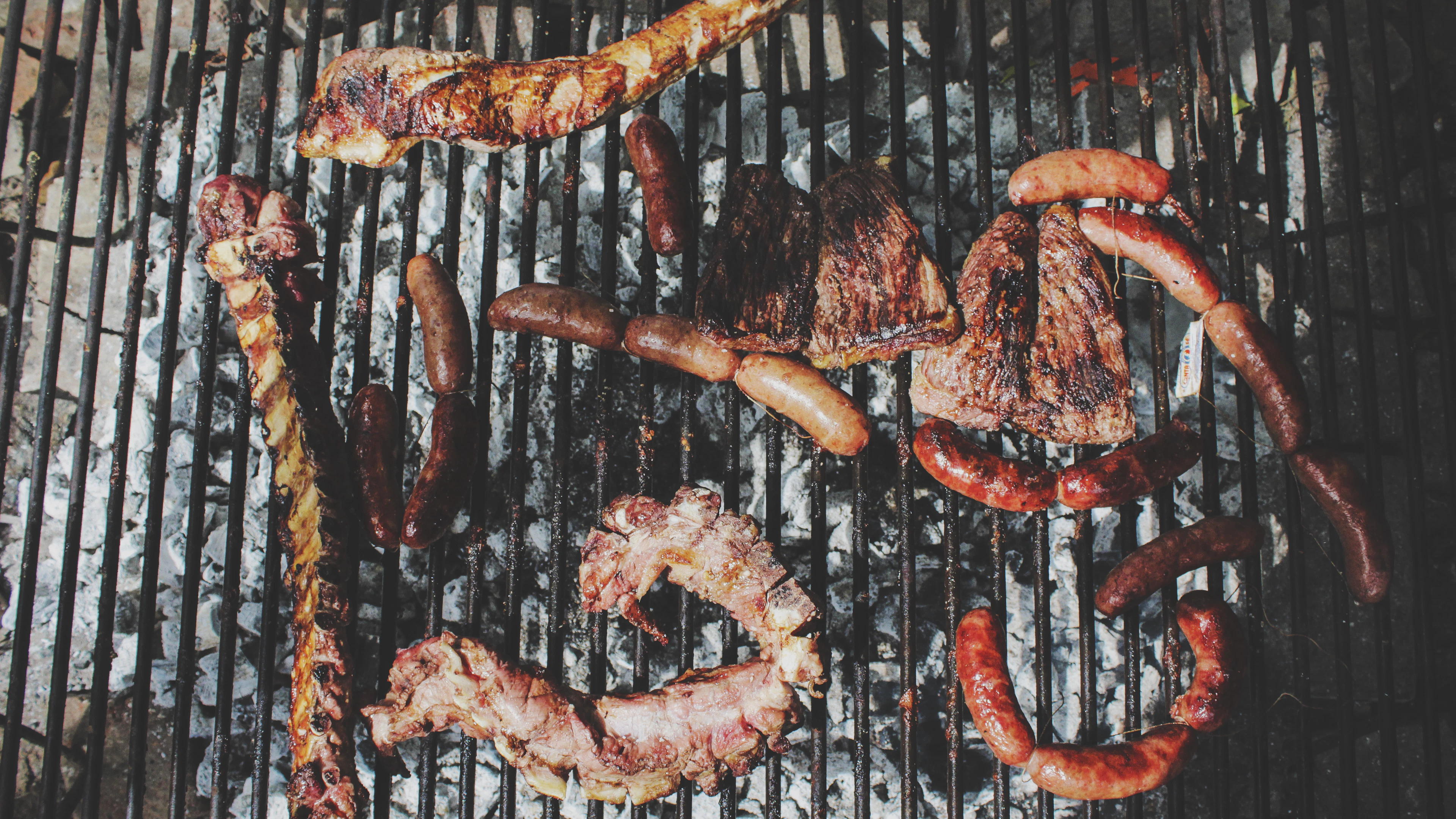 Sausages and cuts of meat cooking over the bars of an open grill