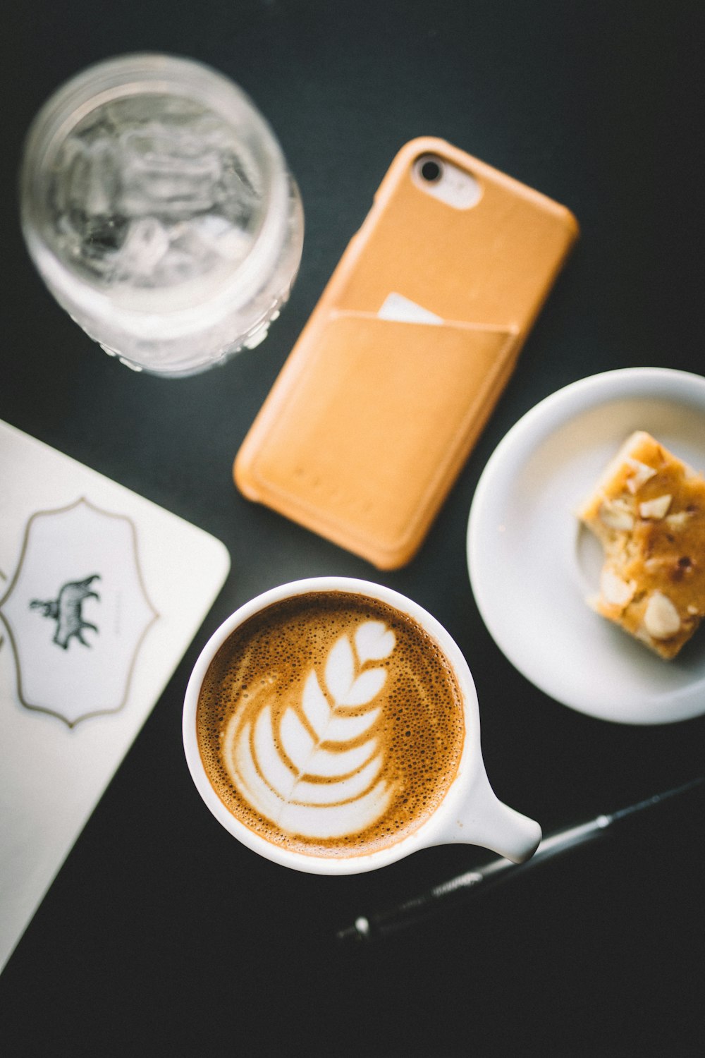 Foto de enfoque selectivo de una taza de capuchino junto al teléfono inteligente, el platillo y el vidrio