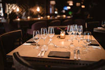 A warmly lit dining table set with fine wine glasses and ivory linens against a matte black backdrop.