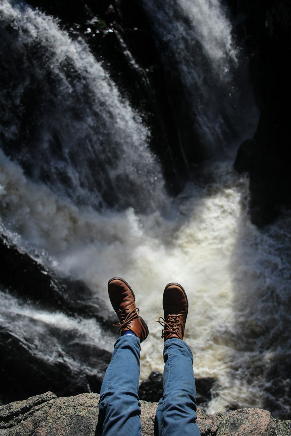 person sitting on rack with waterfalls during daytime