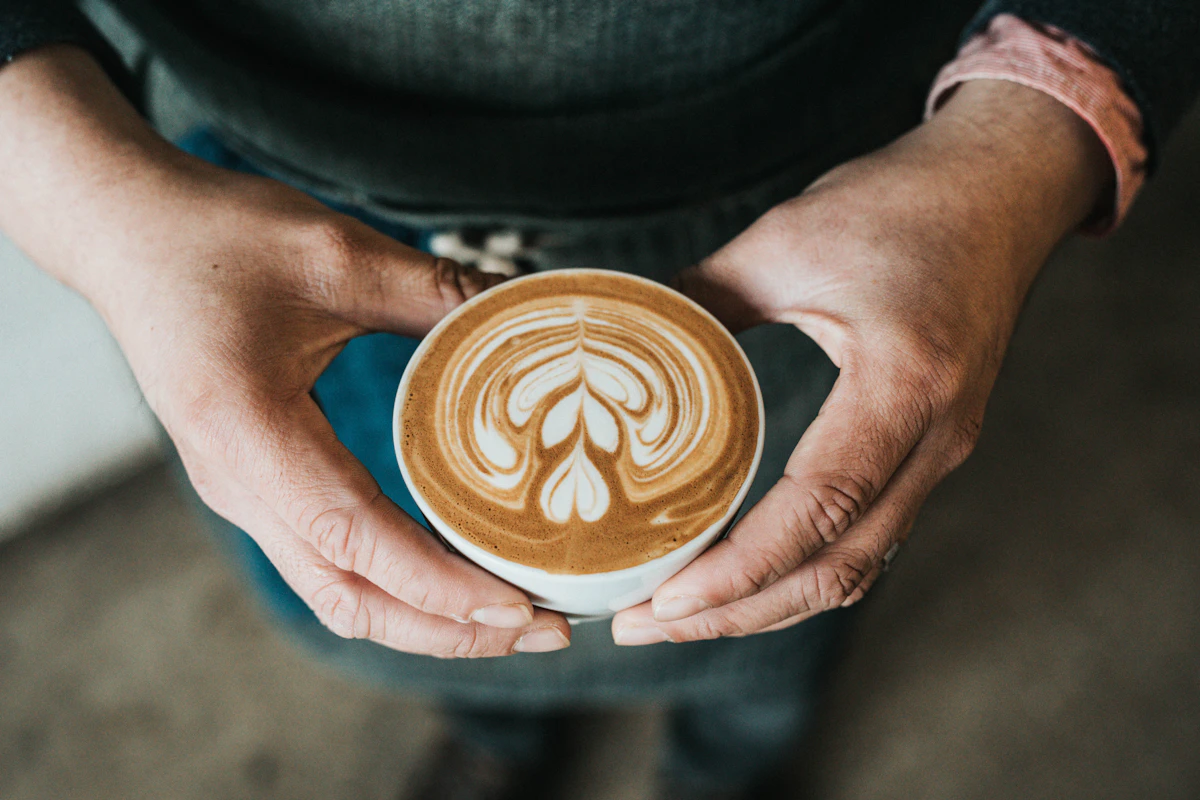 A barista's hands presenting a cup of coffee with latte art
