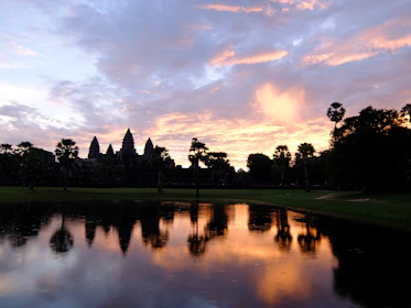 Ancient temples of Angkor Wat glowing warmly at sunset, surrounded by lush greenery.