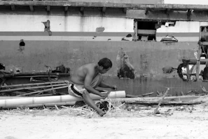 Hands sanding down a broken surfboard, surrounded by scraps and sandpaper in a small workshop.