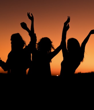 silhouette of three woman with hands on the air while dancing during sunset